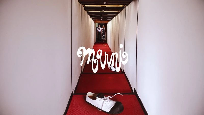 Fashion editorial shot in a hallway with a white and black shoe, two figures in the background and the Marni brand logo.