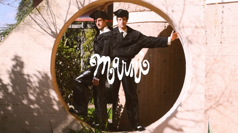 Two adult males in formal wear posing in a round concrete archway. Outdoor fashion shot with shadows and an illustration overlay.