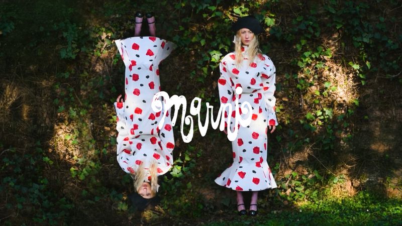 Two adult females wearing white dresses with red dots and black hats in a forest, one is upside down reflecting a mirrored composition.
