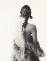 Model from behind with a long braided hairstyle wearing a textured feather garment against a plain white background