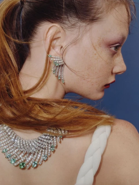 Elegant jewelry on a fair-skinned adult female with red hair pulled back, showcasing a necklace and earrings against a blue background.