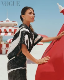 Antonela Roccuzzo in a black and white textured dress standing on a sandy beach for Vogue Latin America editorial
