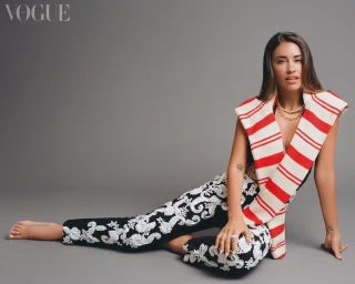 Antonela Roccuzzo wearing patterned trousers and draped red-and-white sweater against a grey studio backdrop