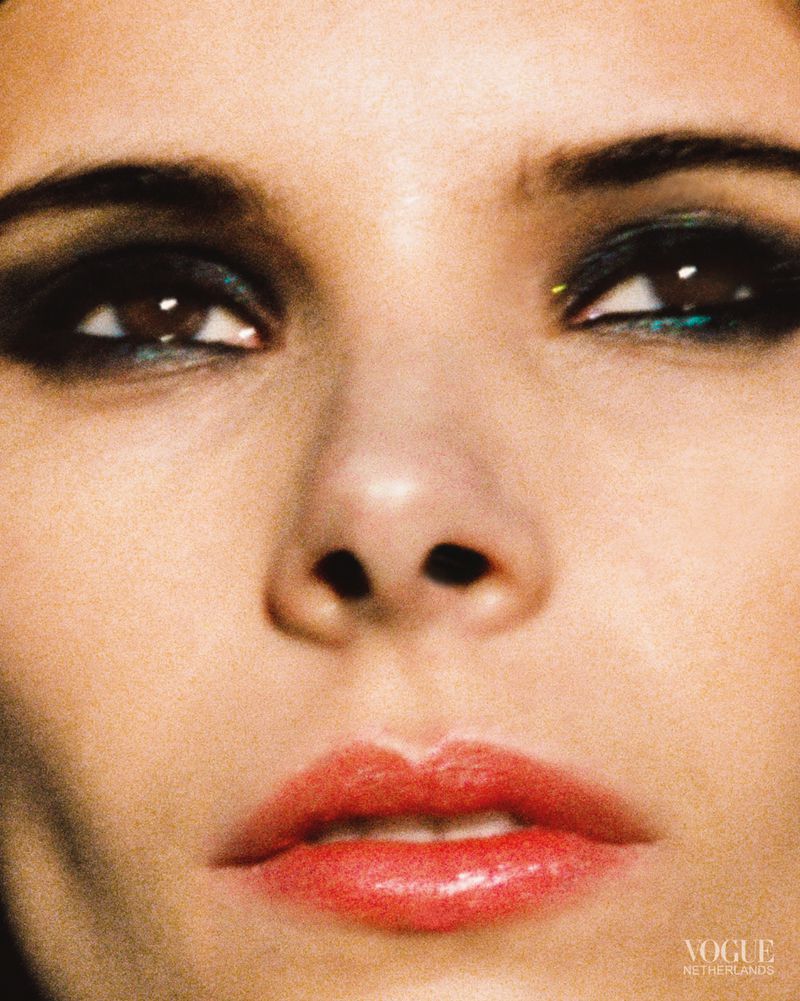 Close-up portrait of a fair-skinned young adult woman with striking makeup, including smokey eye shadow and bright coral lips, for beauty advertisement.