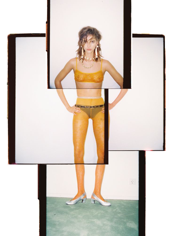 A fashion shot of a woman in a yellow bra and hosiery posing in front of stacked polaroid frame collages against a bright background.