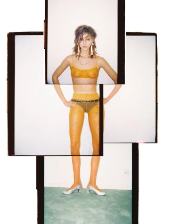 A fashion shot of a woman in a yellow bra and hosiery posing in front of stacked polaroid frame collages against a bright background.