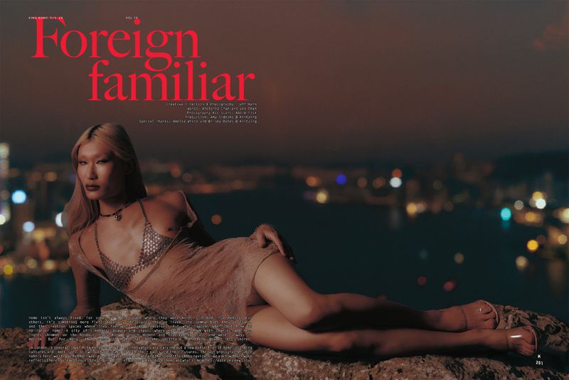 Asian female model poses on a rock in a sheer dress with city lights in the background for a fashion editorial.