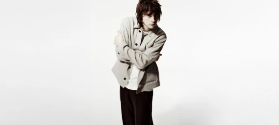Gene Gallagher in a light jacket and dark trousers standing against a plain white studio backdrop.