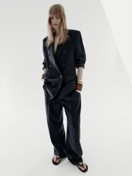Model wearing a dark oversized double-breasted suit and chunky bangles against a neutral background
