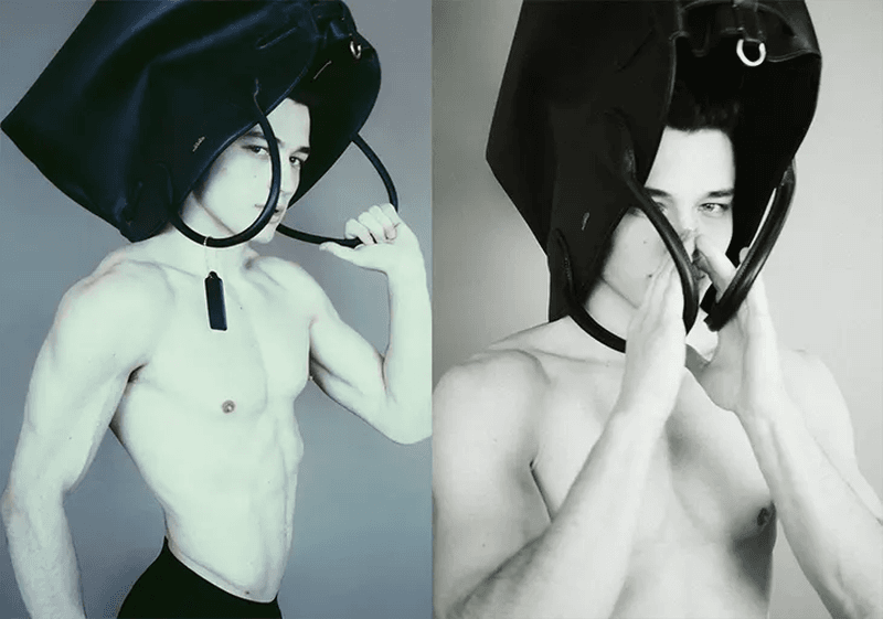 A man with athletic physique poses in a studio setting with a large black bag covering his head, showcasing a unique fashion-forward style.