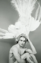 Monochrome portrait of a seated man wearing an elaborate white feathered headpiece for Dreaming Awake