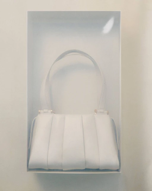 White fashion handbag with top handle displayed in a clear plastic case, studio shot. Luxury fashion accessory in a display box.