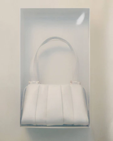 White fashion handbag with top handle displayed in a clear plastic case, studio shot. Luxury fashion accessory in a display box.