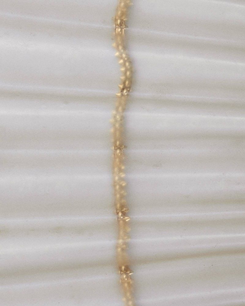 Close-up shot of a delicate gold necklace with small embellishments, displayed on a smooth, textured off-white fabric surface.