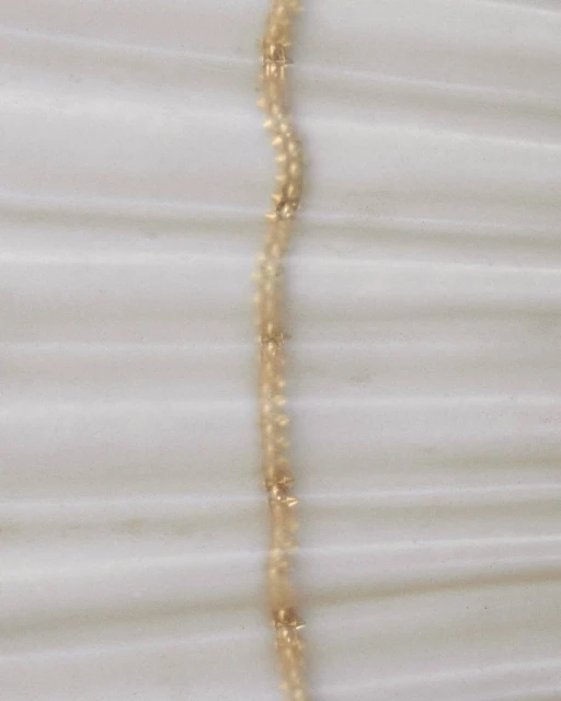 Close-up shot of a delicate gold necklace with small embellishments, displayed on a smooth, textured off-white fabric surface.