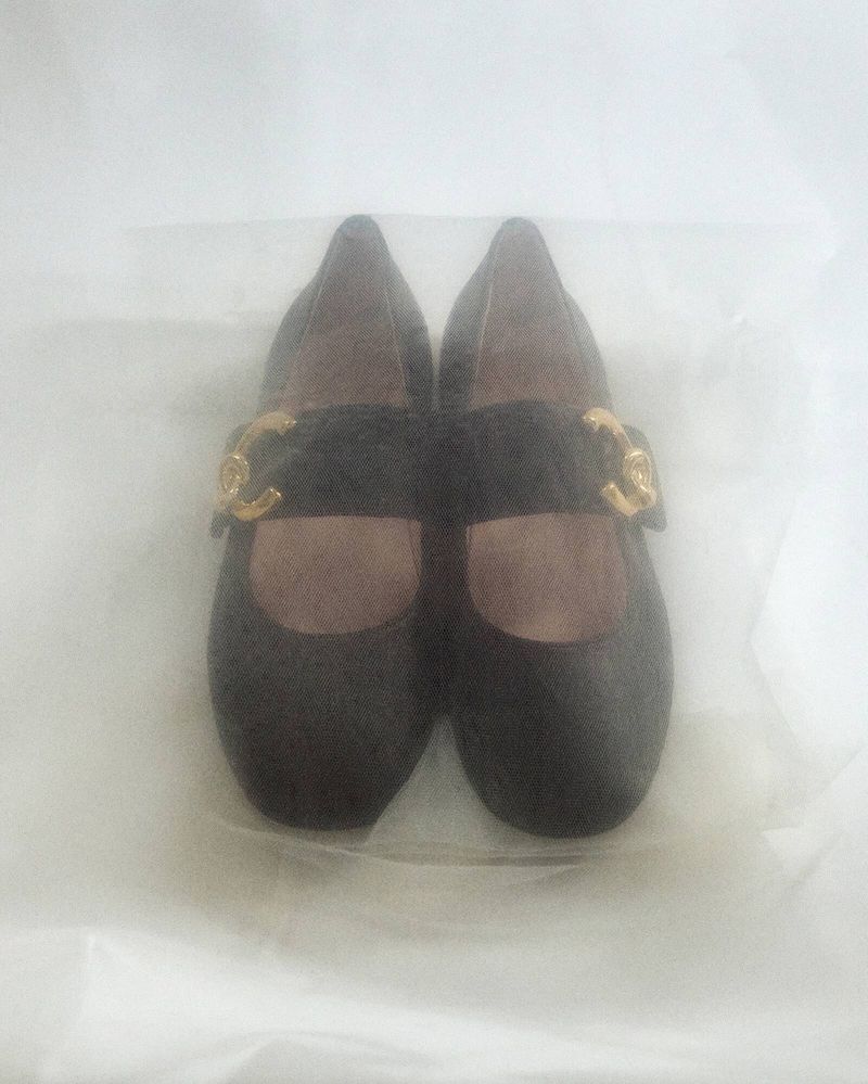 Black Mary Jane shoes with gold hardware buckles on a white surface, close-up product shot showcasing the footwear's design and details.