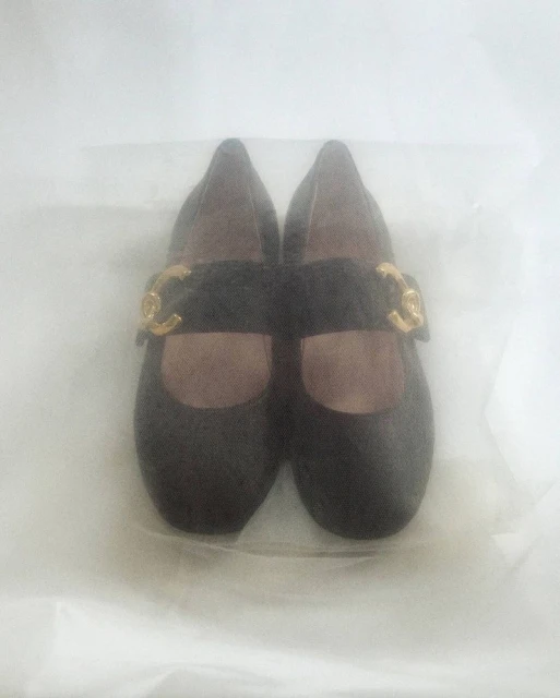 Black Mary Jane shoes with gold hardware buckles on a white surface, close-up product shot showcasing the footwear's design and details.