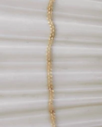 Close-up macro shot of a delicate gold beaded chain resting against a white pleated background for D Repubblica.
