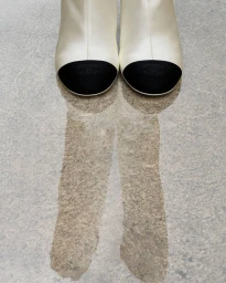 Close-up of cream white boots with black toes standing on a textured stone ground reflecting shadows.