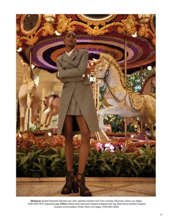 Elegant woman in tailored suit on carousel. Dark-haired model in gray coat and skirt poses in front of decorated horses and foliage.