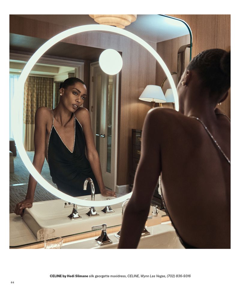 Woman in black dress reflected in illuminated mirror in a luxurious bathroom. Fashion shot with high-end interior design elements.
