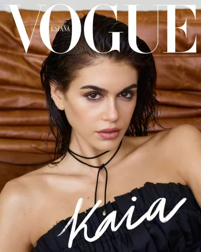 Close-up portrait of model Kaia Gerber with wet hair wearing a black strapless top and thin black choker necklace against leather background