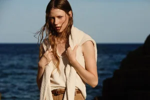 Model with long wet-look hair wearing a cream knit sweater by the ocean for Seventy Spring Summer 25 campaign