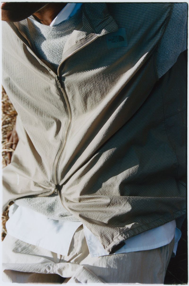 Tan zip-up jacket and neutral-toned apparel, top-down shot on a person outdoors. Soft lighting shows details of the clothing textures.