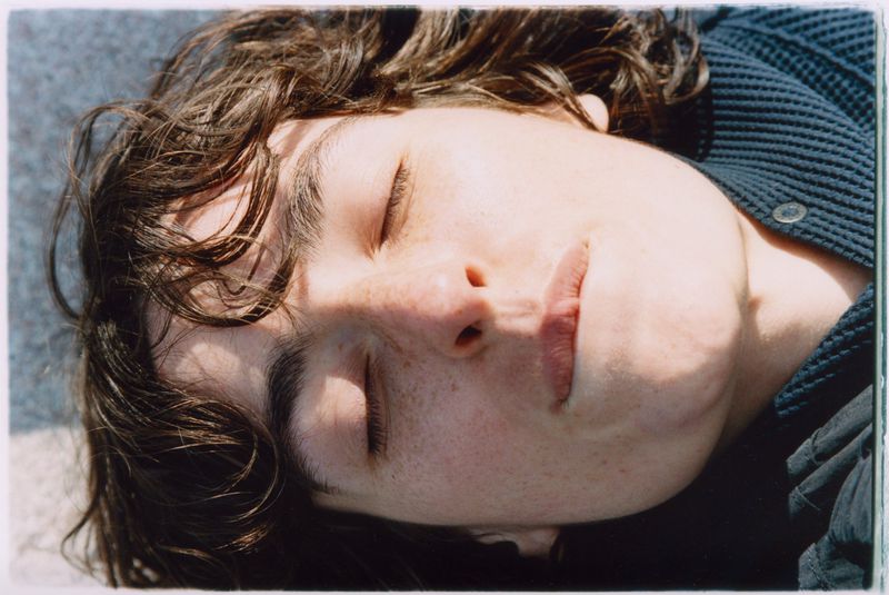 Close-up portrait of an adult female with wavy brown hair, lying down with her eyes closed, wearing a navy blue waffle knit shirt.