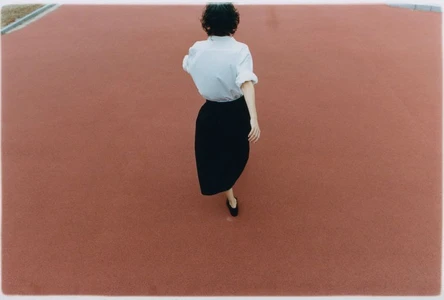 High angle shot of a person walking on a red running track wearing a white shirt and black skirt