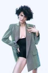 Woman with short dark hair wearing a metallic green blazer and black bodysuit against a white background