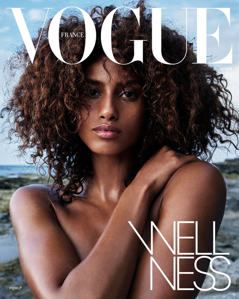 Close-up fashion magazine cover featuring a single tanned-skin adult female model with curly brown hair, gazing intensely at the viewer.