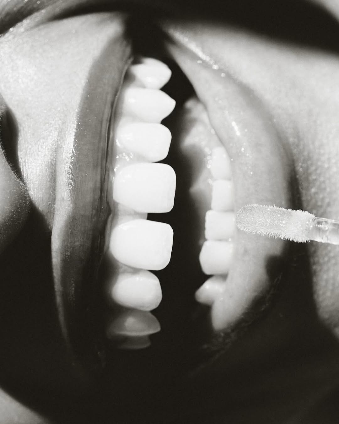 Open mouth close-up with teeth, gums, and a small swab, captured in a black and white studio shot, emphasizing dental care and hygiene.
