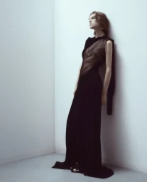 Model leaning against a corner wall wearing a long black dress for Peter Do Spring 2024 campaign