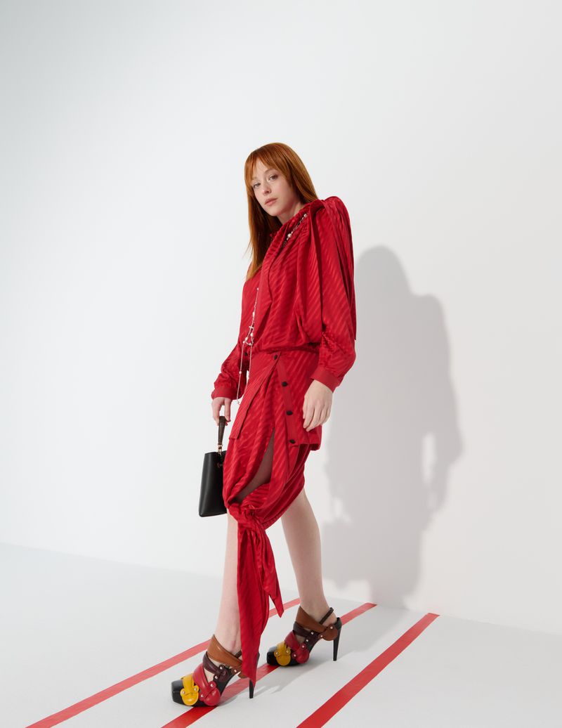 Fashionable woman in a red patterned dress and colorful heels poses against a bright white background in a studio setting.