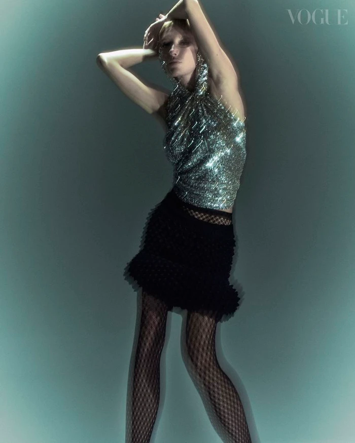 Model in glittering halter top and black miniskirt posing against a glowing teal backdrop with motion blur effect