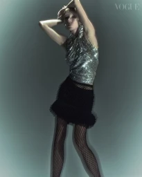 Model in glittering halter top and black miniskirt posing against a glowing teal backdrop with motion blur effect