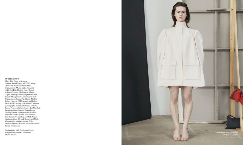 Full-shot studio fashion portrait of a model wearing a short, light pink dress with puffed sleeves, standing against a gray background.