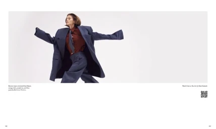 Model in an oversized blue blazer, orange shirt, tie, and trousers against a white backdrop