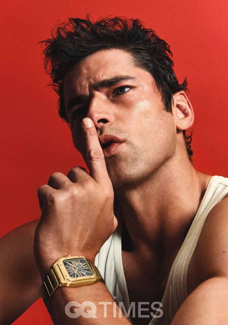 Portrait of a man with a gold watch holding a finger to his lips against a red background, looking toward the light source.