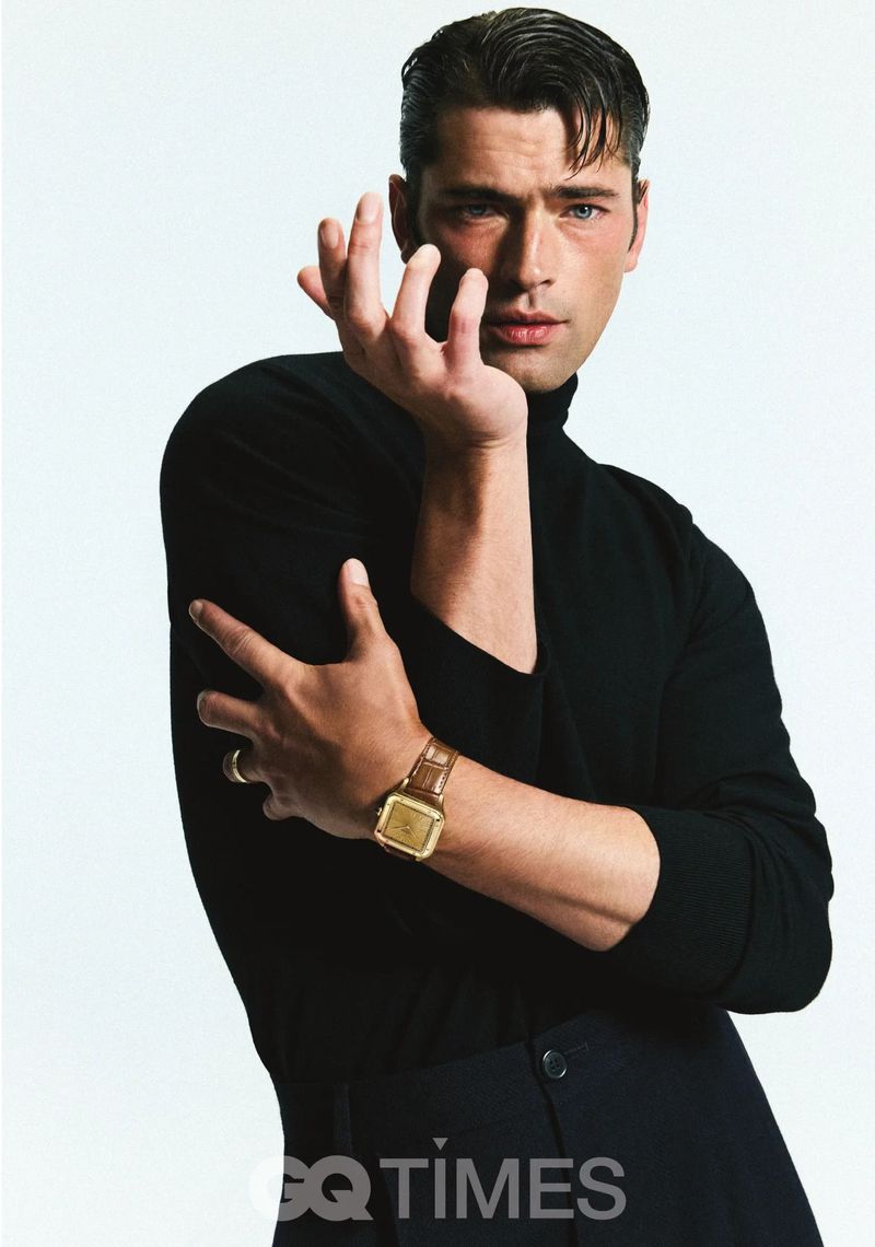 Portrait of a handsome adult male model wearing a black turtleneck and a gold watch, posing against a bright white studio backdrop.