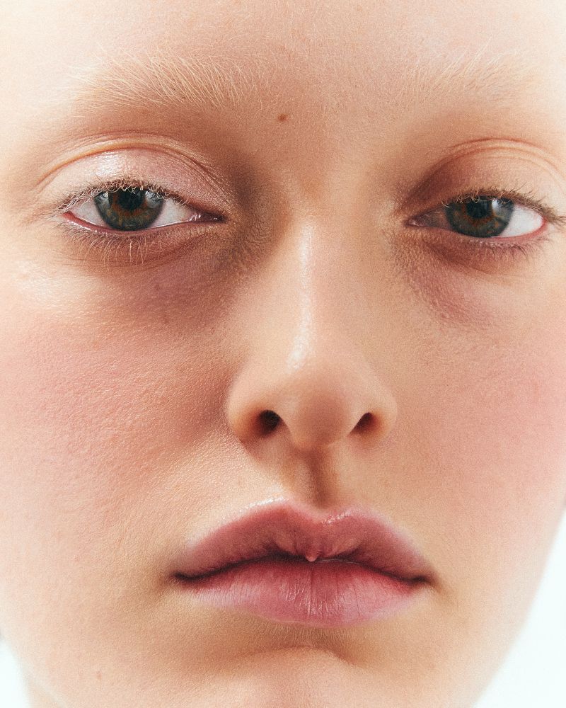 Close-up portrait of a fair-skinned adult female with light blonde hair, light eyebrows, and brown eyes. Soft, diffused lighting.