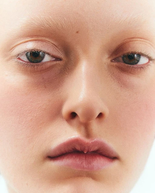 Close-up portrait of a fair-skinned adult female with light blonde hair, light eyebrows, and brown eyes. Soft, diffused lighting.