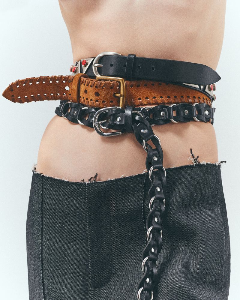 Close-up of a torso wearing a deconstructed denim skirt and accessorized with layered leather belts in black and brown colors.