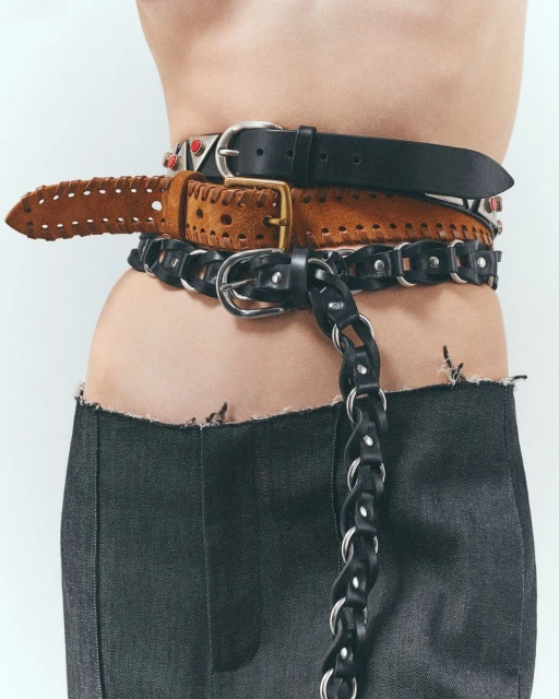 Close-up of a torso wearing a deconstructed denim skirt and accessorized with layered leather belts in black and brown colors.