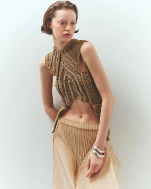 Model wearing a textured brown knit sleeveless top and pleated skirt against a plain background