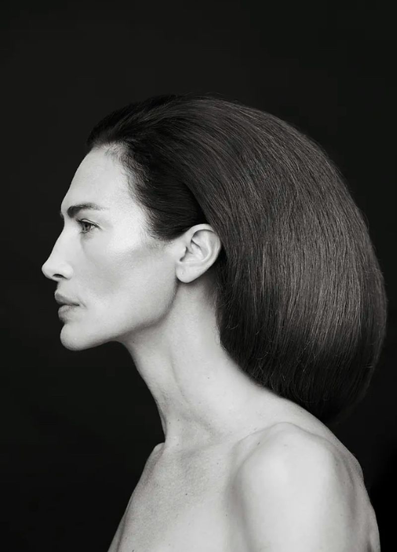 Monochrome portrait of an adult woman in profile with dark hair against a dark background. Minimalist studio headshot.