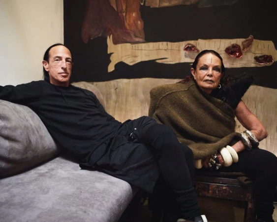 Rick Owens and Michele Lamy seated together on a grey sofa against a dark painted backdrop for L'Etiquette Magazine.
