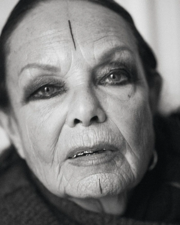 Close-up portrait of Michele Lamy in black and white with a vertical line tattoo on her forehead and chin