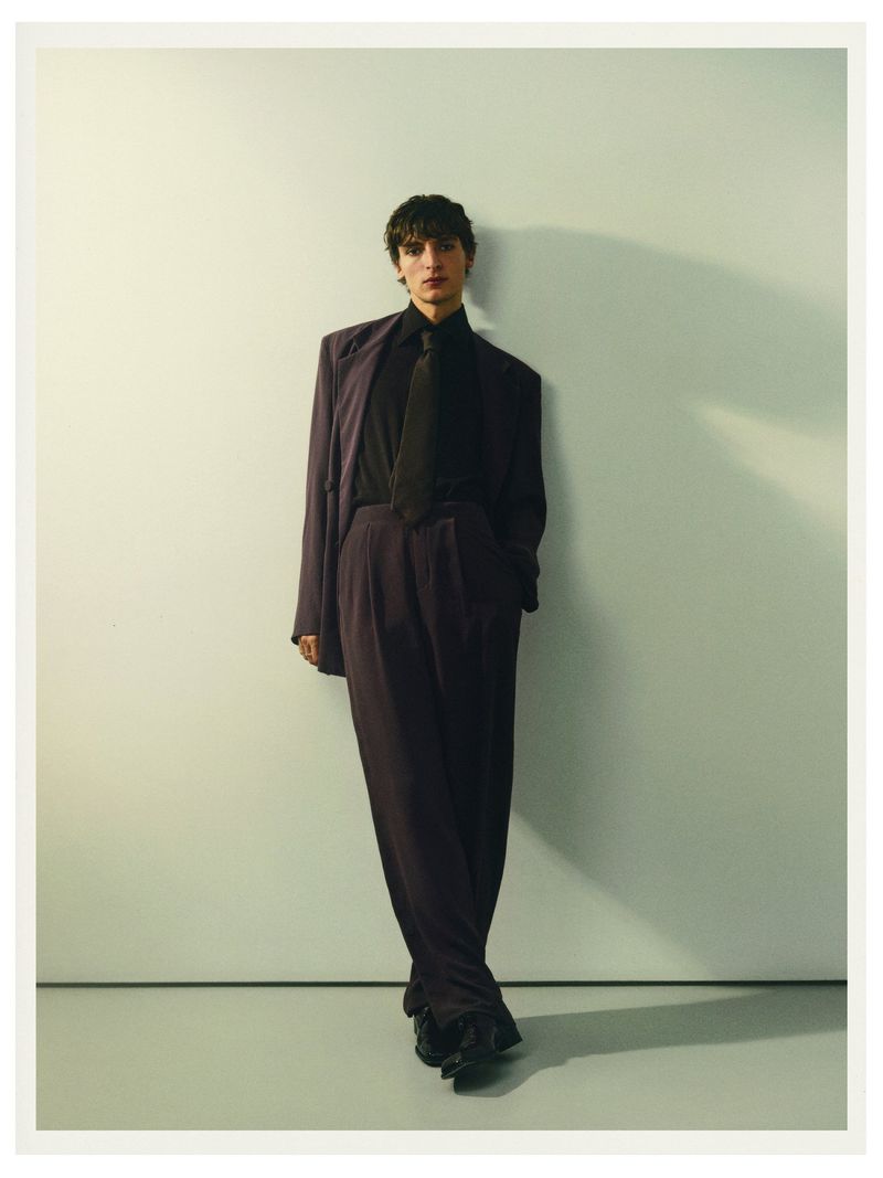 Model Vassili Schneider in dark suit and tie leaning against a pale studio wall for Silhouette Magazine portrait